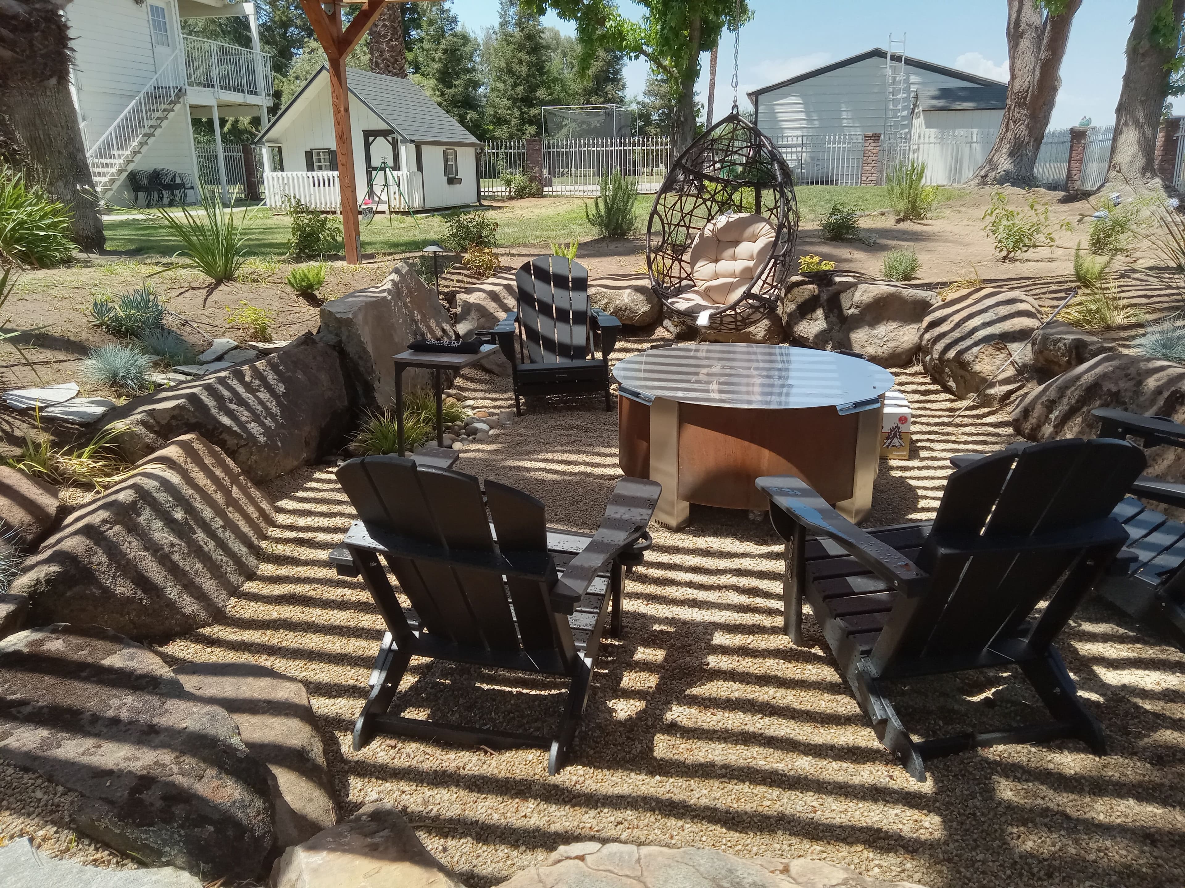 Cozy outdoor seating area with black Adirondack chairs and a circular coffee table in a landscaped garden.
