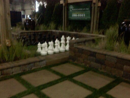 Giant white chess pieces beside a landscaped garden with stone walls and ornamental plants.