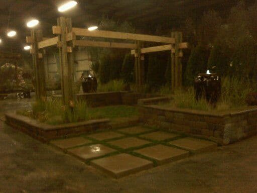 Outdoor garden structure with wooden pergola, stone pathways, and decorative planters.