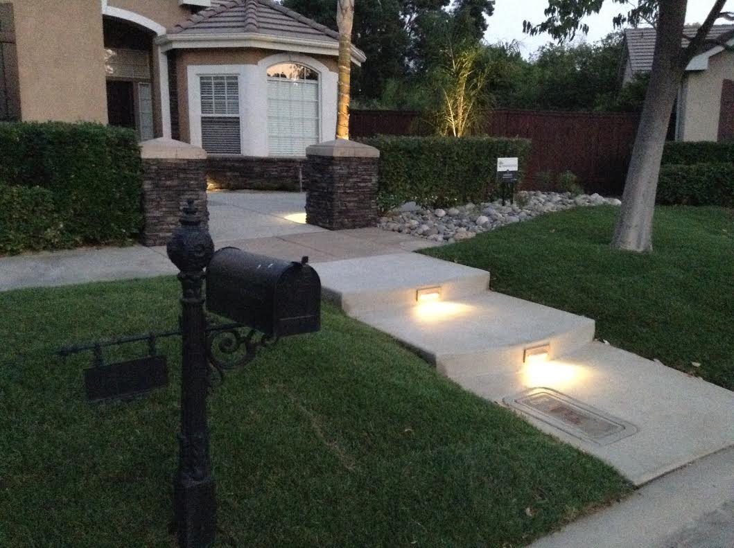 Illuminated pathway leading to a home with landscaped greenery and decorative mailbox.