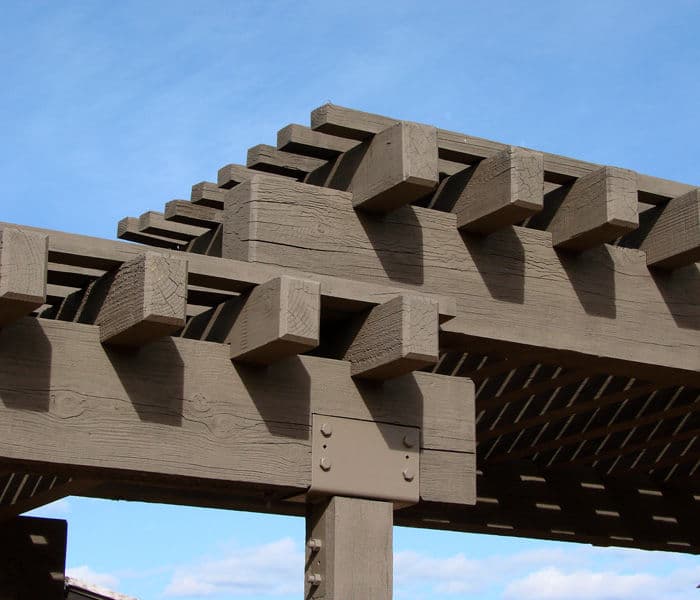 Wooden pergola structure with detailed beams against a blue sky. Ideal for outdoor spaces.