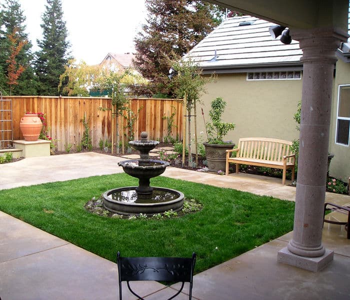 Serene backyard garden with fountain, green lawn, bench, and wooden fence.