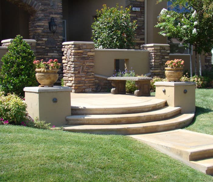 Elegant stone staircase with planters leading to a landscaped entryway. Lush greenery surrounds.