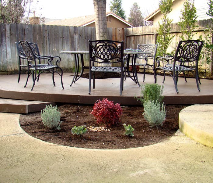 Outdoor patio with black metal chairs and tables surrounded by landscaped shrubs.