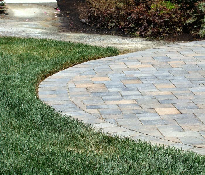Curved stone pathway bordered by lush green grass in landscaped garden.