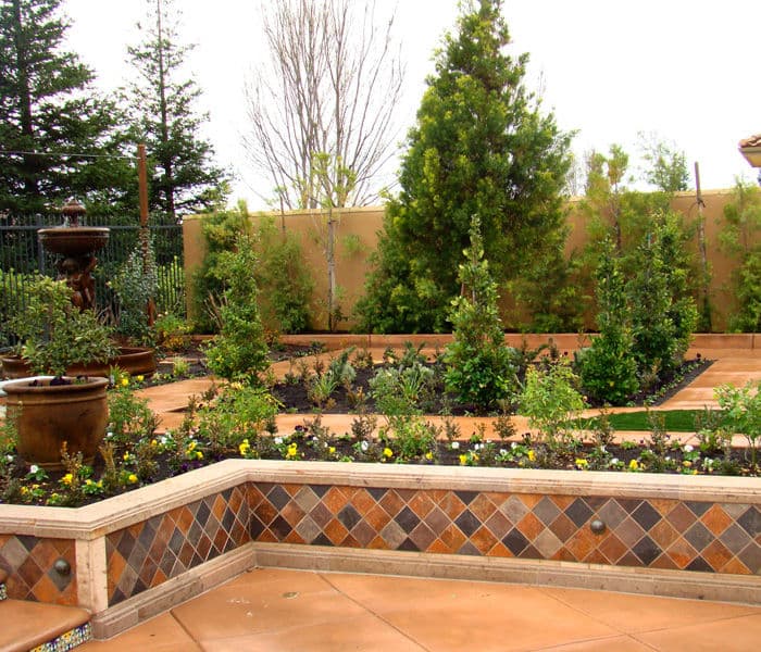 Lush garden landscape featuring neatly arranged trees, plants, and decorative stonework.