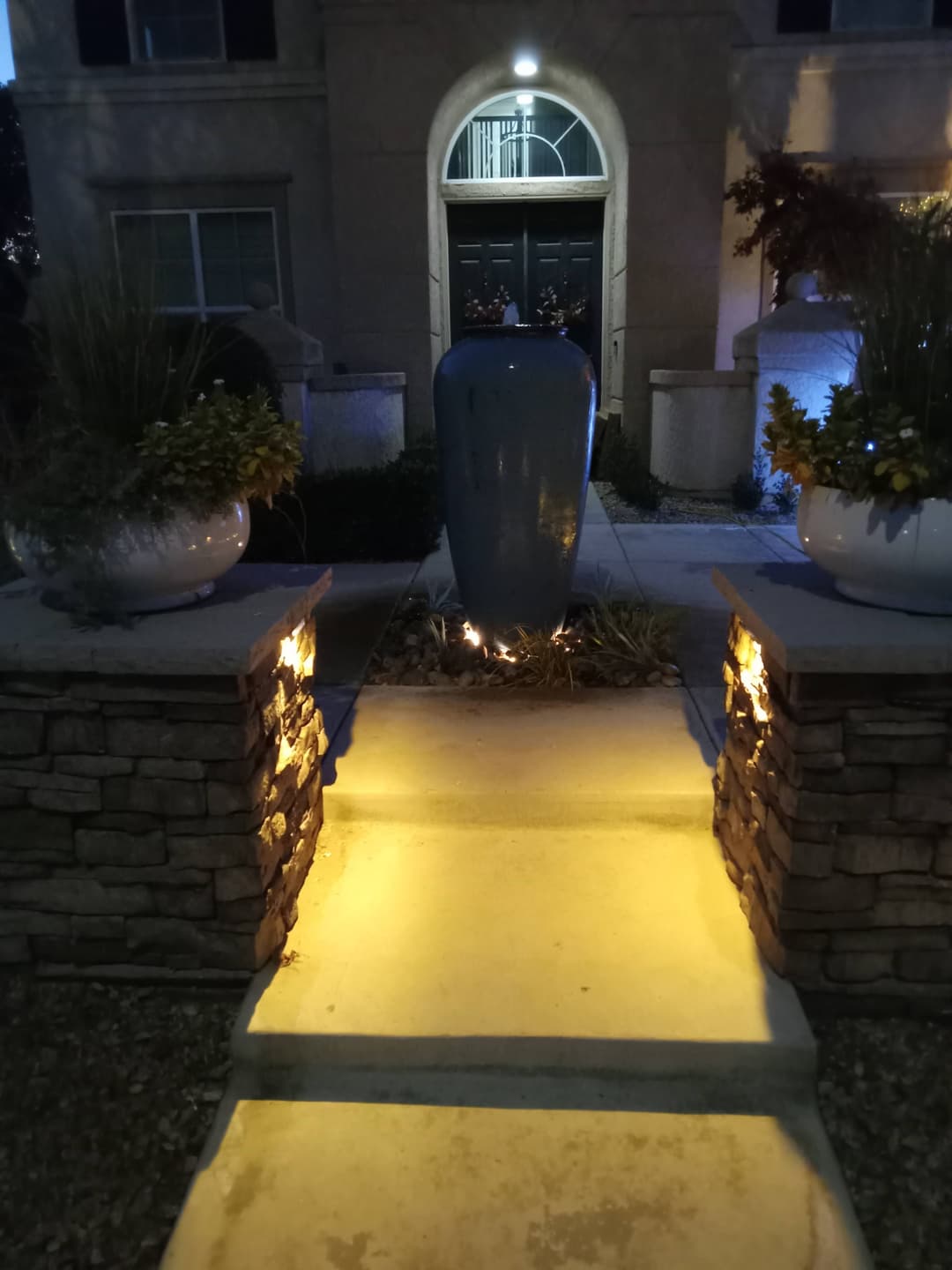 Elegant blue vase centerpiece by a well-lit stone pathway leading to a residential entrance.