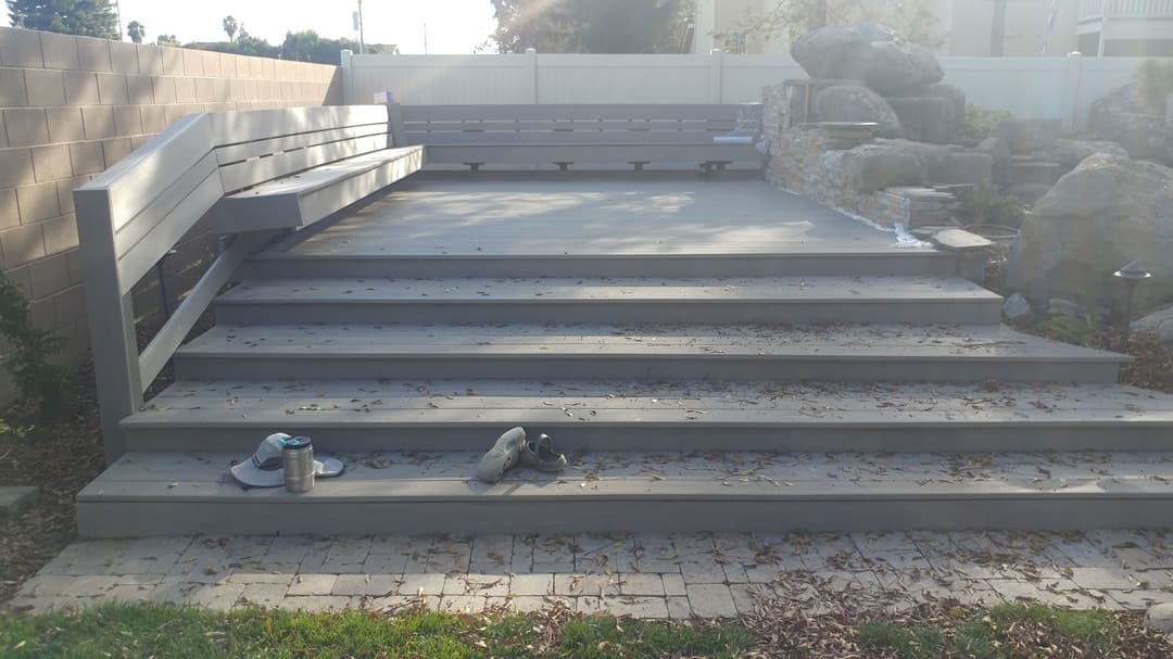 Wooden deck with steps, surrounded by rocks and shrubs, featuring casual footwear.