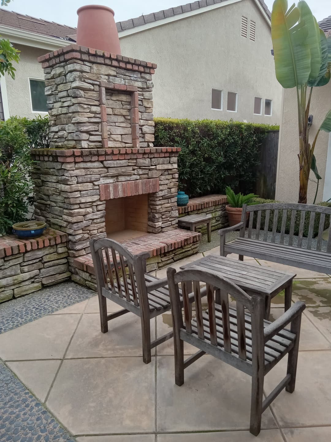 Outdoor stone fireplace with wooden seating in a landscaped patio area.