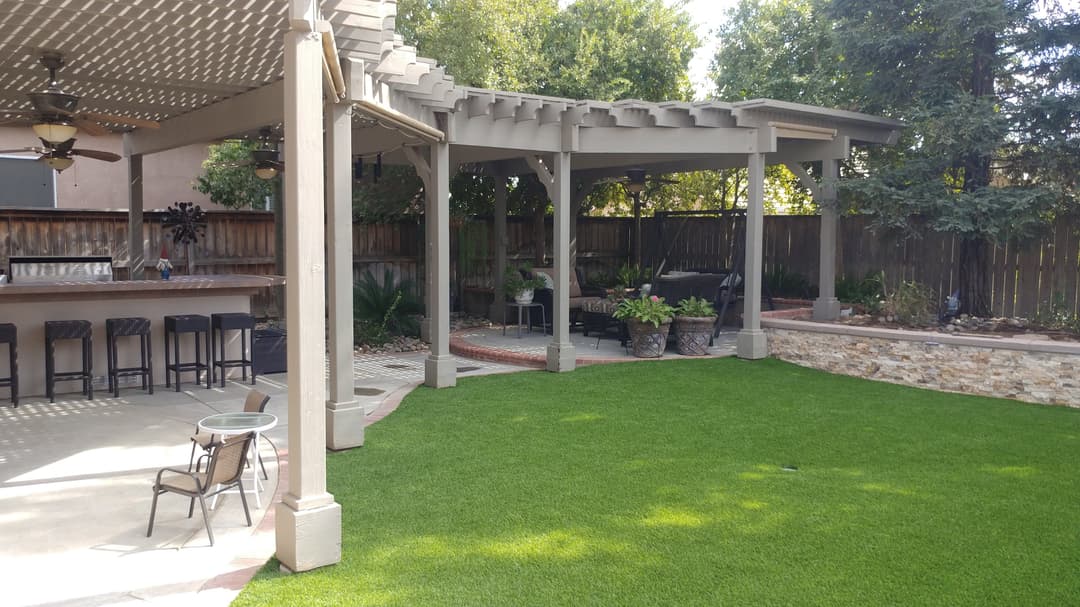 Lush backyard with artificial grass, patio area, and shaded seating under pergola.