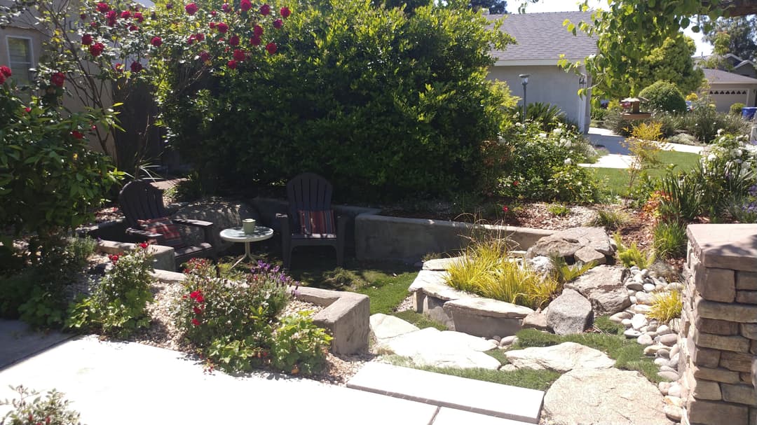 Lush garden with seating area, water feature, and vibrant flowers in a serene outdoor space.