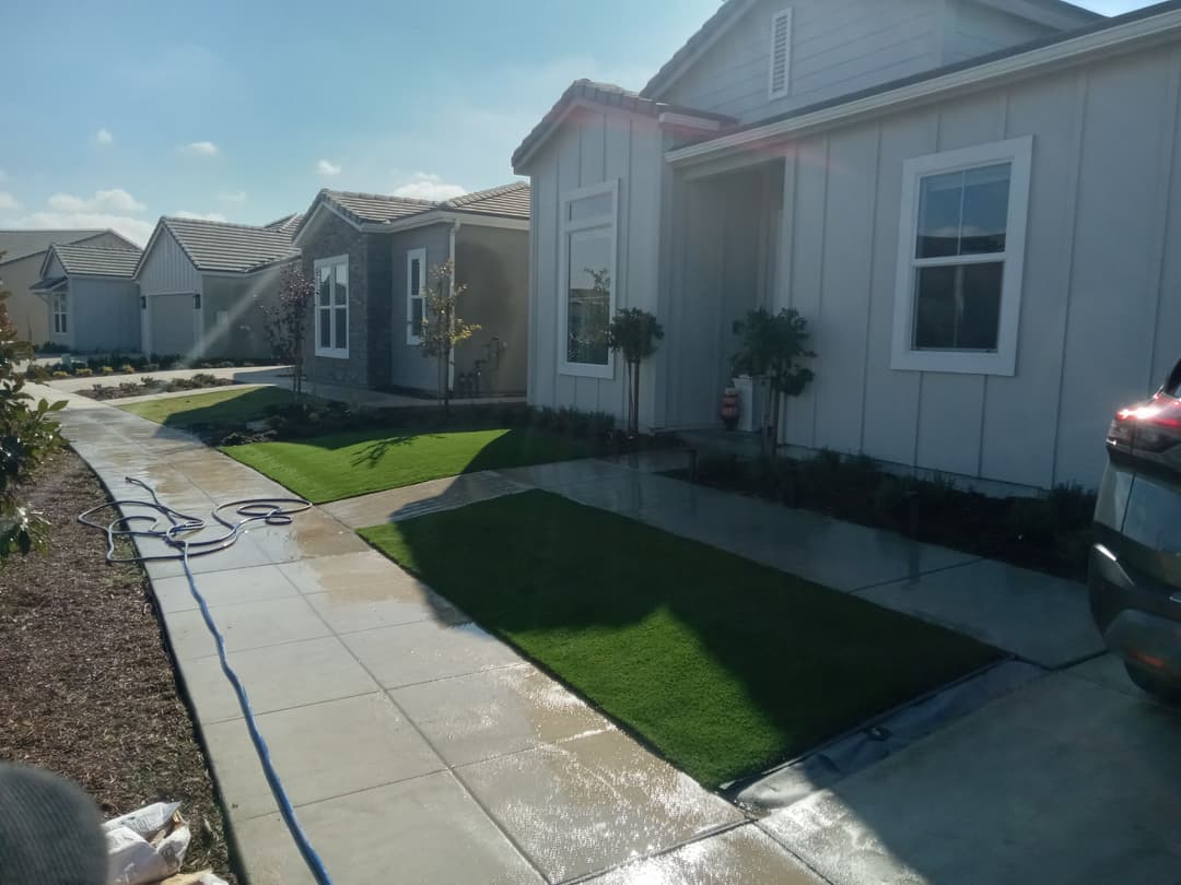 Well-maintained front yard with artificial grass and new homes under a clear blue sky.