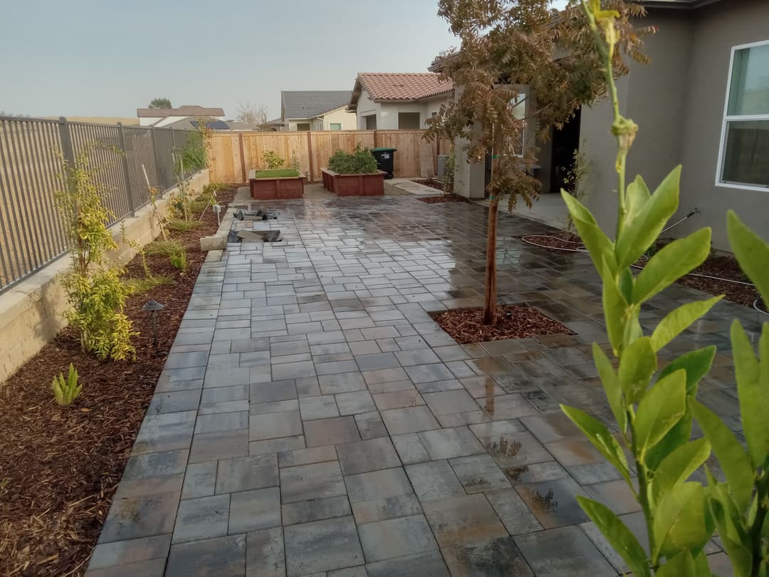 Modern garden landscape with paved walkway, planters, and fresh greenery.