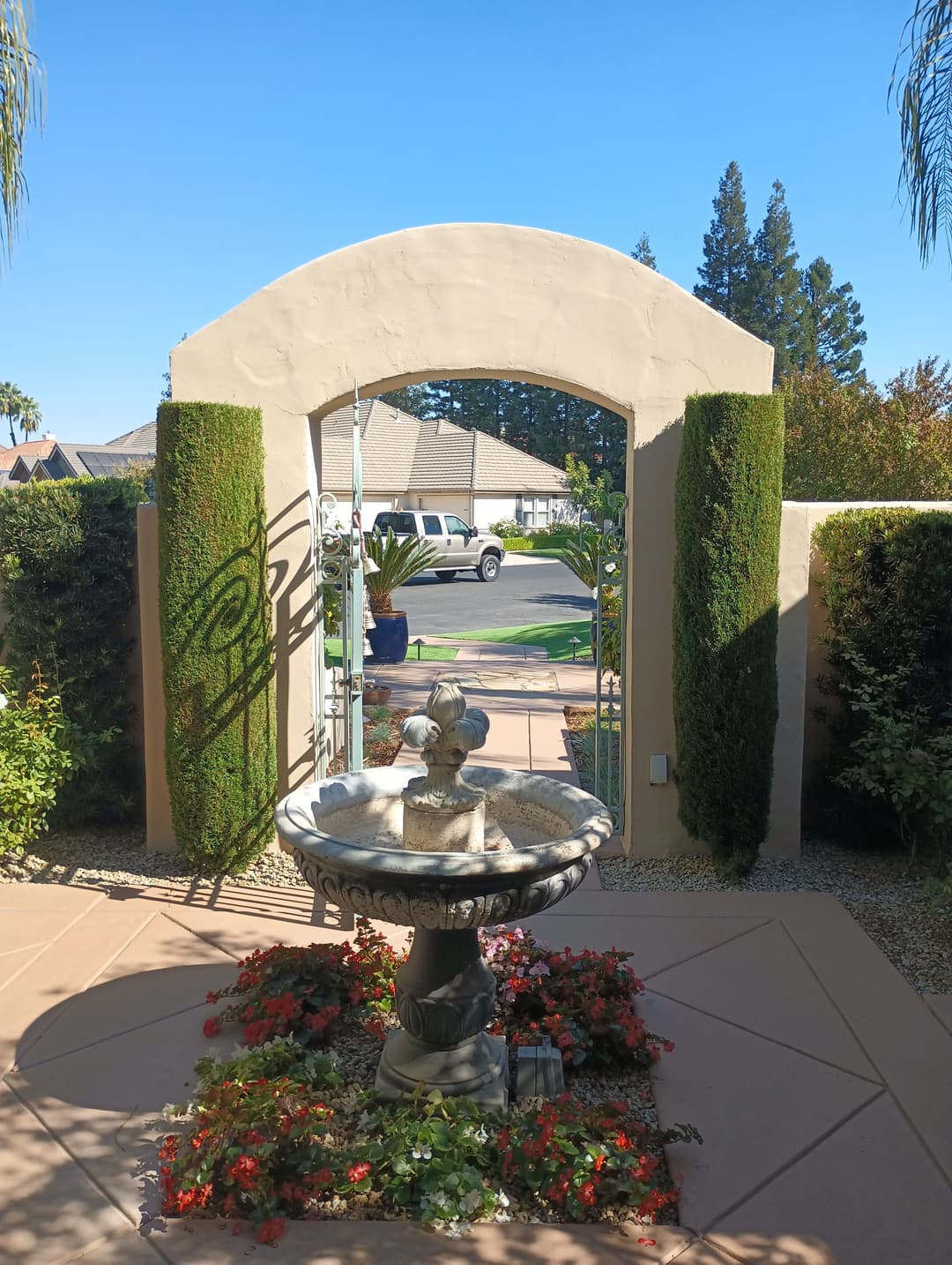 Stone fountain surrounded by flowers at an archway entrance to a garden.