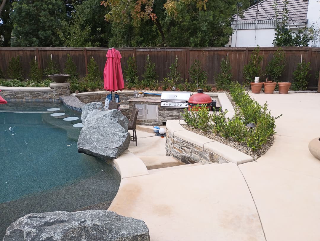 Backyard oasis with pool, stone features, red umbrella, and outdoor grill. Serenity and style.