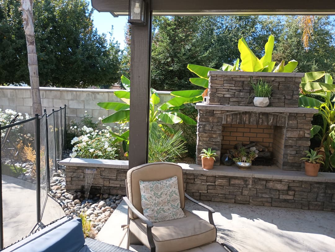 Outdoor patio featuring a stone fireplace, lush greenery, and a cozy seating area.