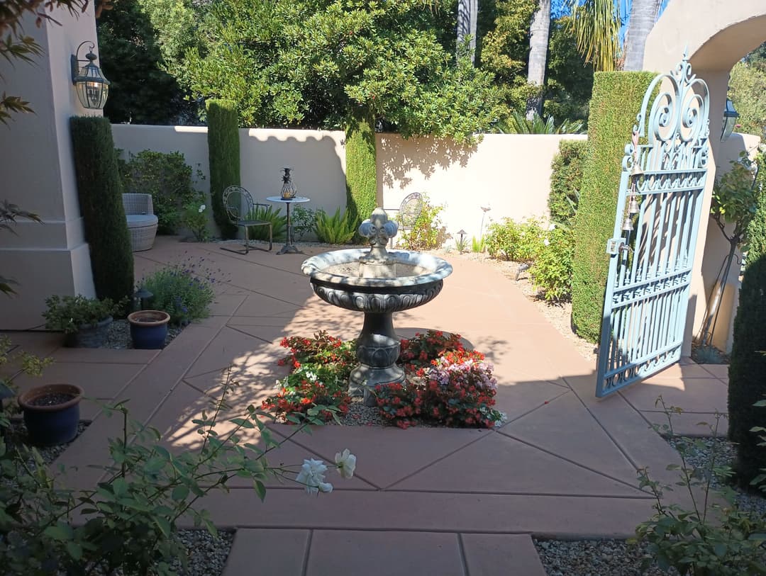 Charming garden oasis featuring a fountain, flowers, and decorative gate surrounded by greenery.