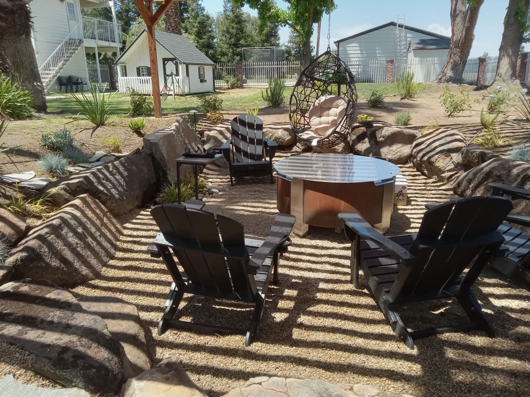 Cozy outdoor seating area with black Adirondack chairs and a circular table surrounded by stone.