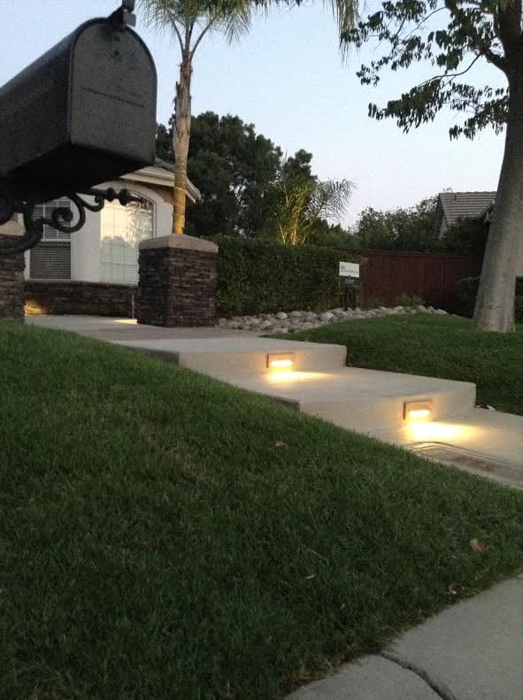 Landscape view of a well-lit walkway leading to a home, with a mailbox in the foreground.