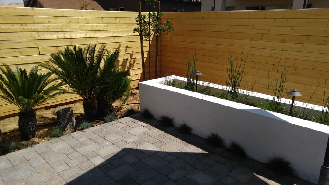 Modern backyard landscape featuring wooden fencing, palm trees, and a white raised planter.