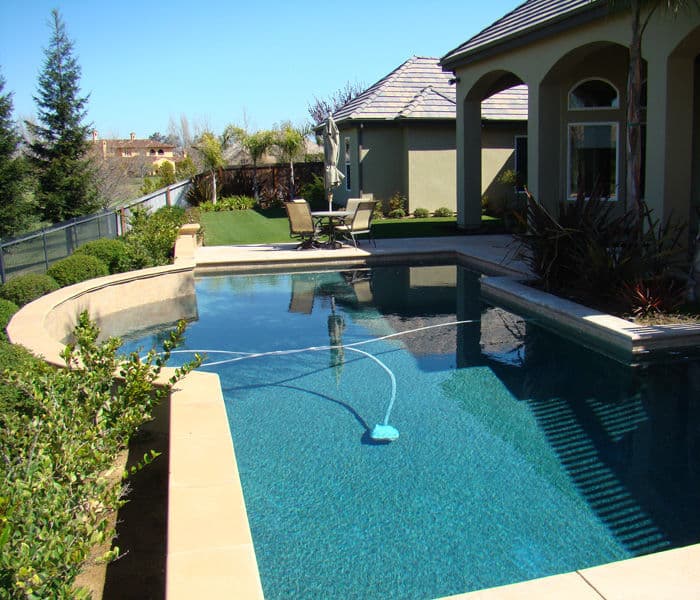 Luxury backyard featuring a clear swimming pool, comfortable loungers, and lush landscaping.