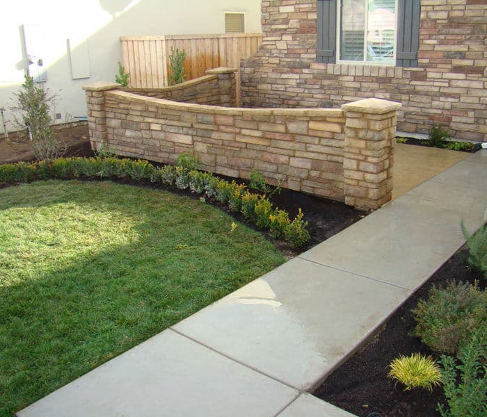 Stone wall garden pathway with lush green grass and neatly trimmed shrubs.