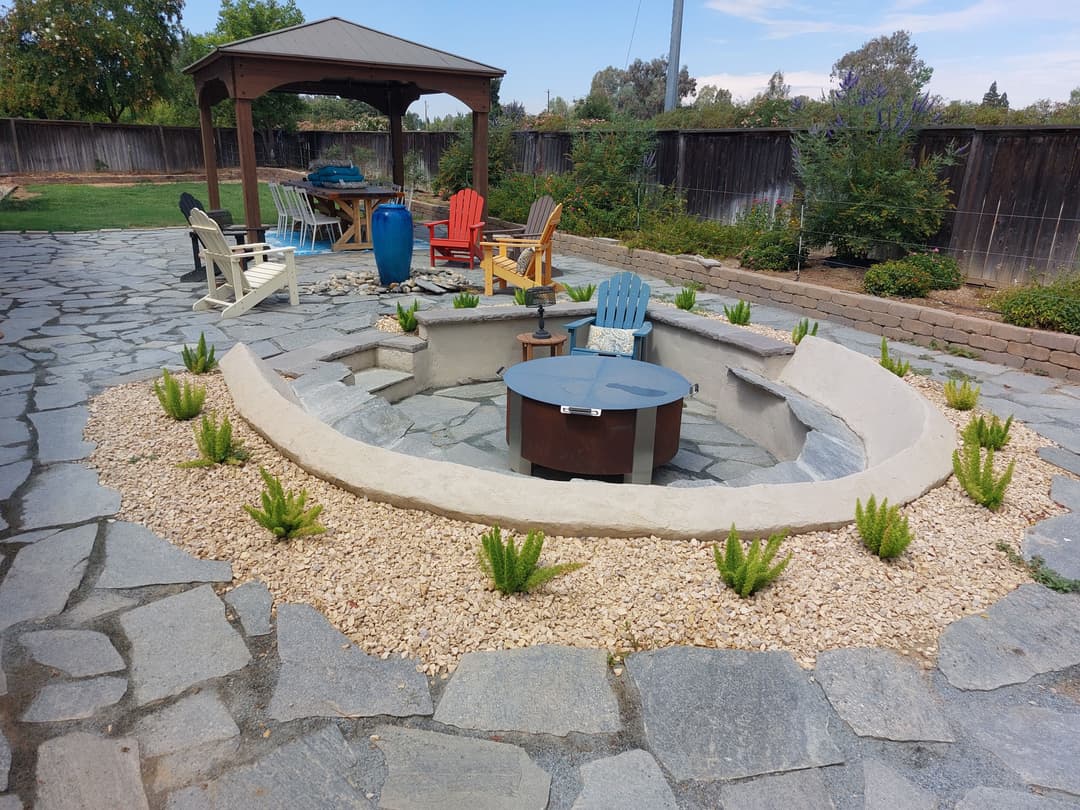 Outdoor seating area with a circular fire pit, stone path, and colorful Adirondack chairs.