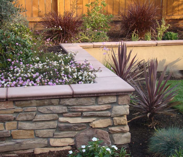 Stone planter with colorful flowers and ornamental grasses in a landscaped garden.