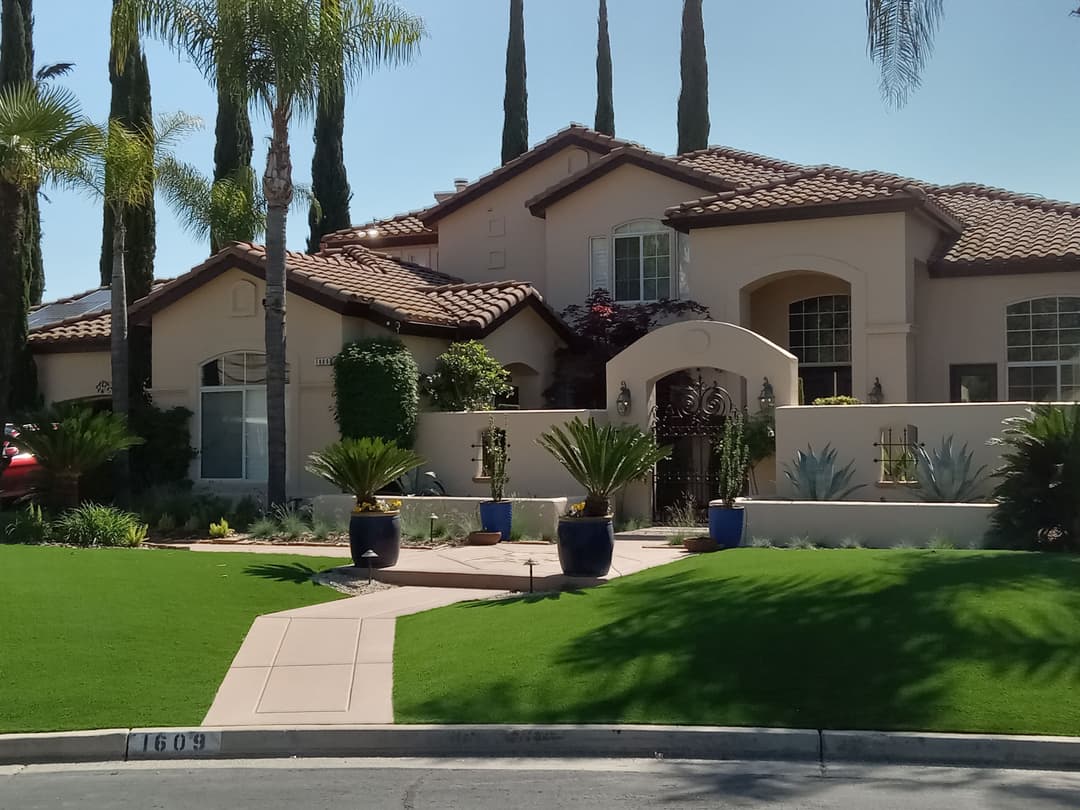 Elegant suburban home with tile roof, lush lawn, palm trees, and vibrant landscaping.