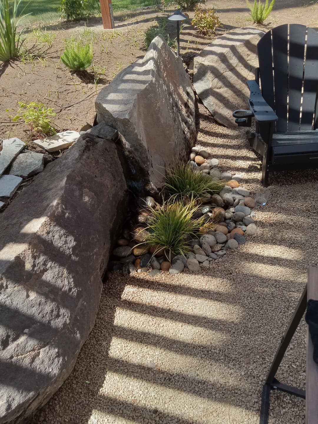 Rock garden with decorative stones, grass, and an Adirondack chair in a serene outdoor setting.