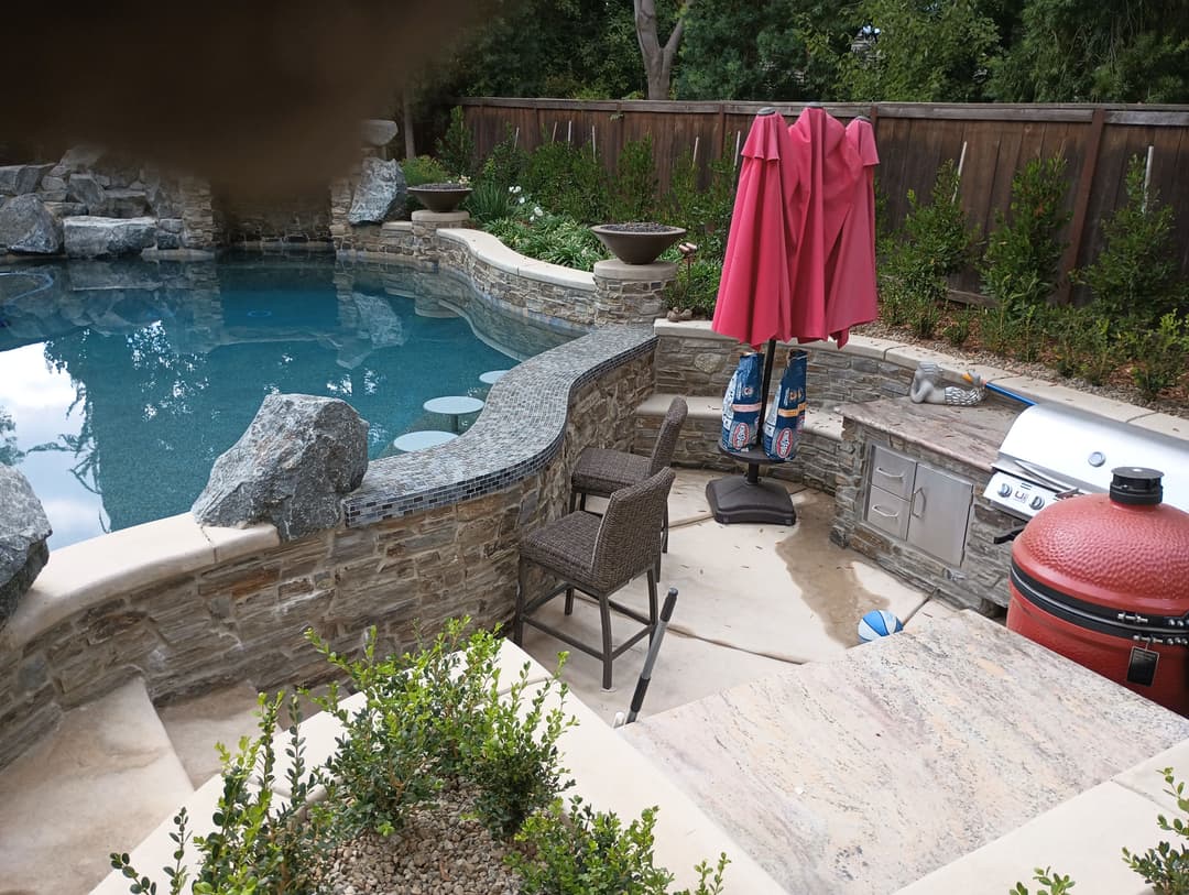 Luxury backyard oasis with a swimming pool, grill station, and red patio umbrella.