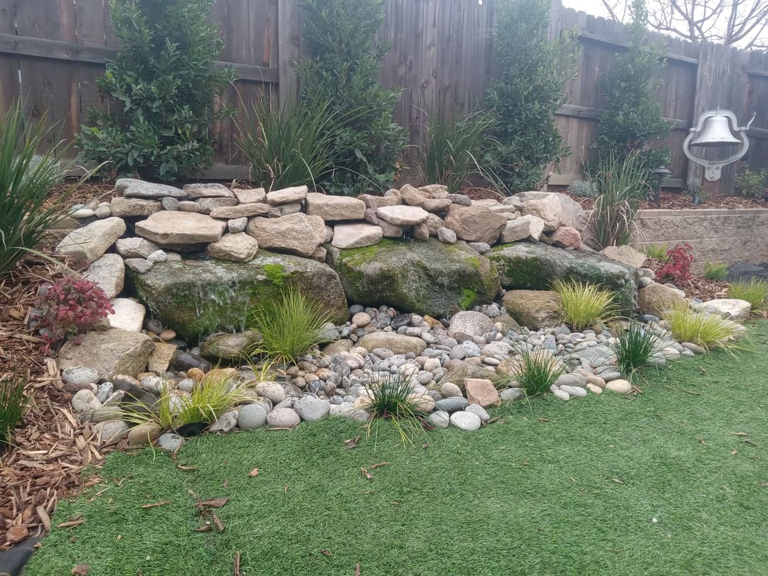 Landscape rock garden with stones, pebbles, and lush greenery in a backyard setting.