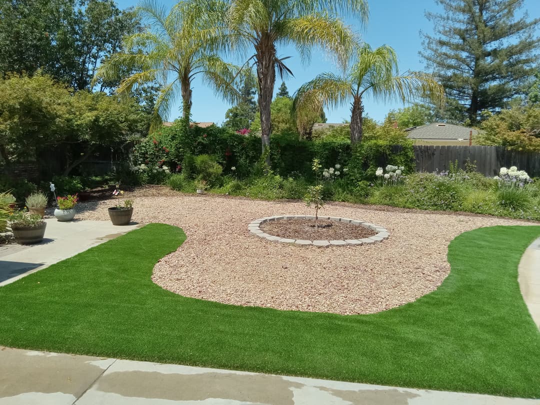 Lush backyard landscape with palm trees, gravel, and circular flower bed centerpiece.