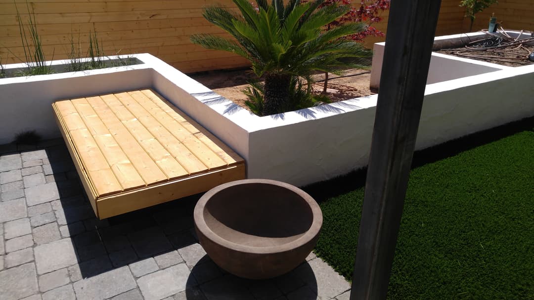 Wooden deck beside a modern garden with palm tree and circular planter in a landscaped yard.