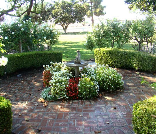 Scenic garden with a stone fountain surrounded by colorful flower beds and lush greenery.
