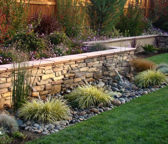 Beautiful landscaped garden featuring a stone retaining wall, decorative rocks, and colorful plants.