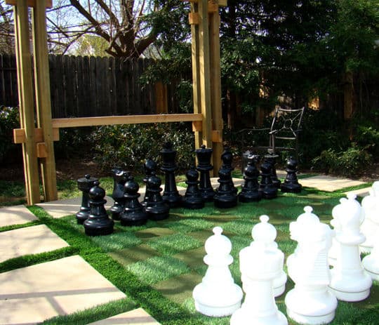 Giant outdoor chess set with black and white pieces on green grass and stone pathway.