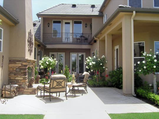 Elegant patio with cozy seating, blooming flowers, and a stone fireplace in a stylish home.