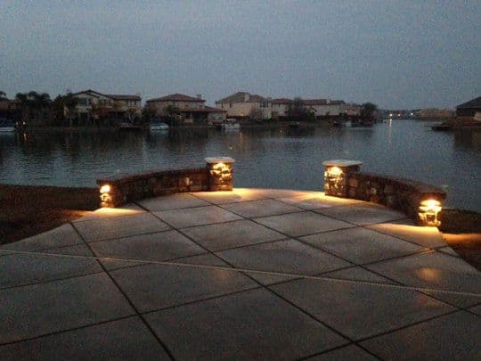 Scenic waterfront patio with stone lighting, overlooking a calm lake at dusk.