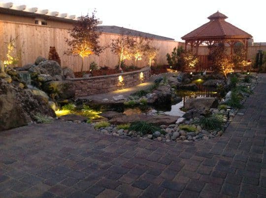 Serene landscaped garden with a pond, gazebo, and illuminated pathways at dusk.