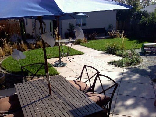 Outdoor patio with a wooden table and chairs under a blue umbrella, featuring a landscaped garden.