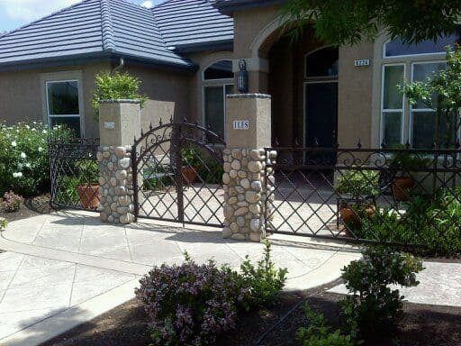 Elegant home entrance with stone and wrought iron gate, surrounded by lush landscaping.