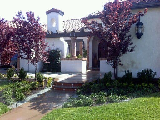 Spanish-style house with lush landscaping and vibrant red maple trees in front garden.