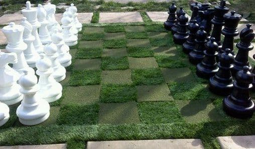 Giant outdoor chess set on grass, featuring white and black pieces in a checkered layout.