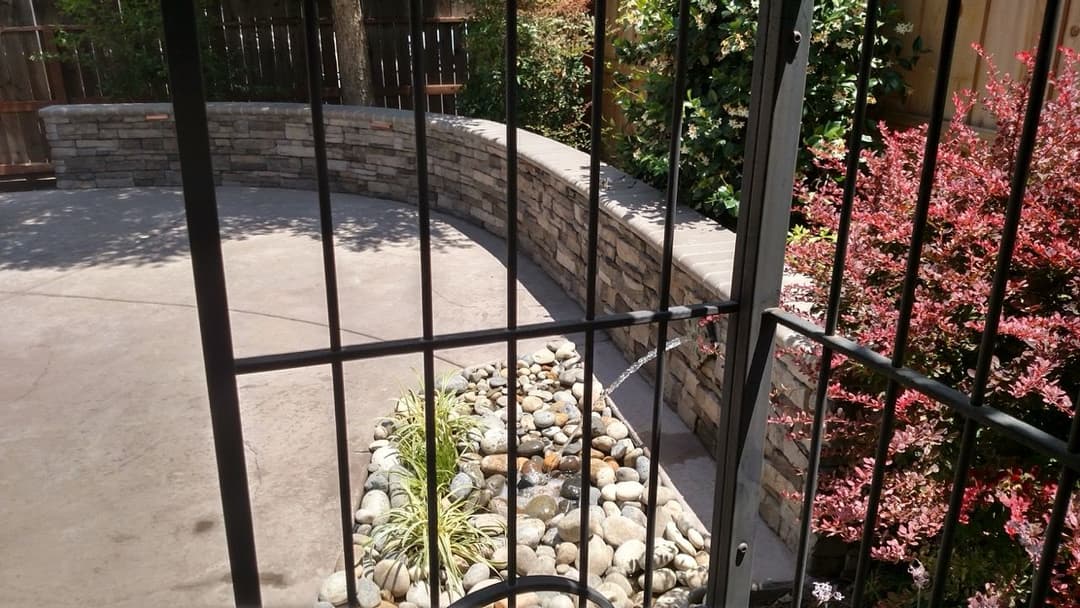 Outdoor garden area featuring a stone wall, decorative plants, and a pebble arrangement.