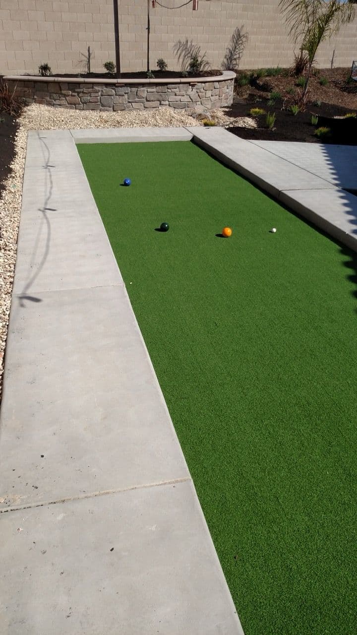 Bocce court with artificial grass featuring blue, green, and orange balls, surrounded by concrete.