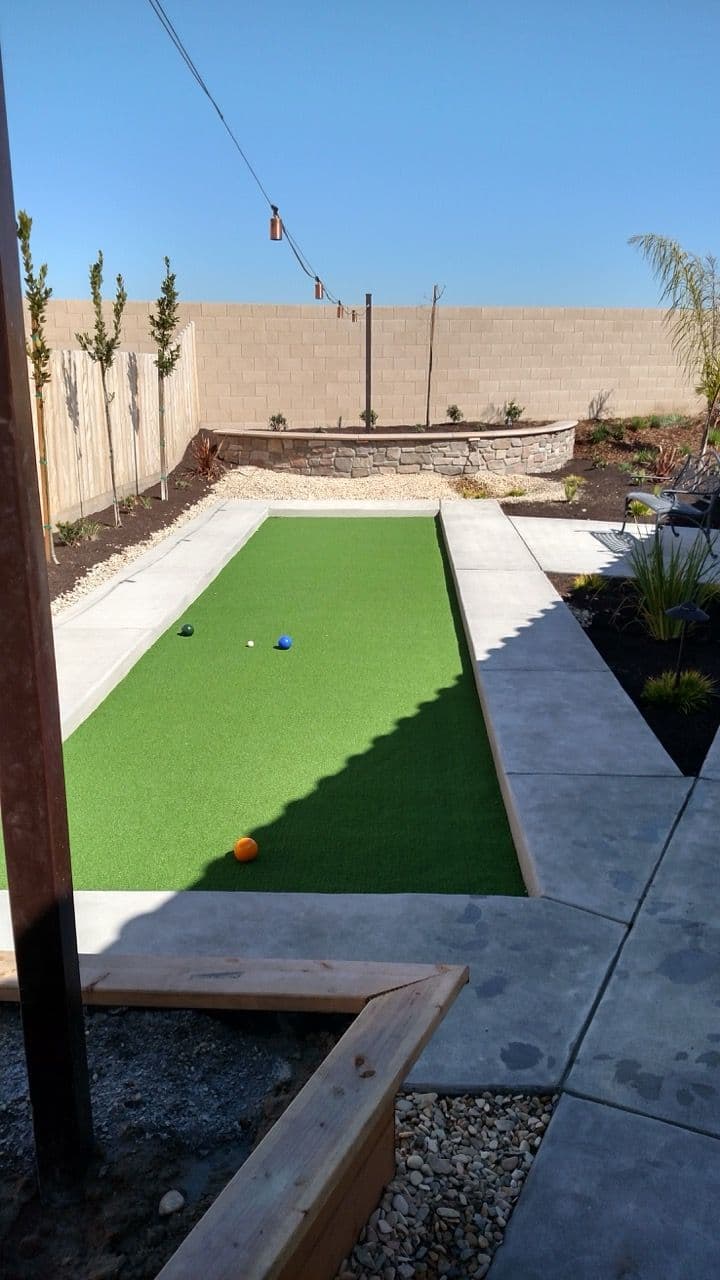 Bocce ball court with artificial turf in a landscaped backyard under clear blue sky.